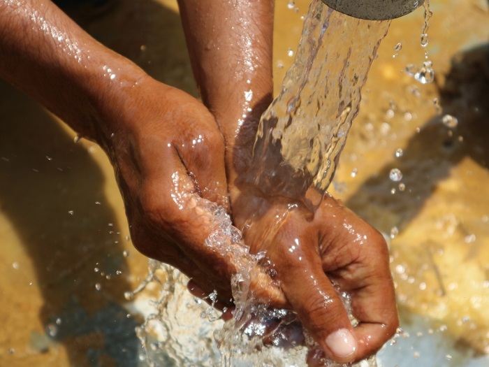 設置されたポンプから出る水で手を洗う人。© Dean Irvine