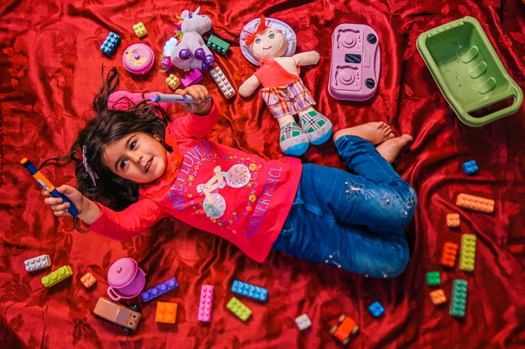 レバノン北部の仮設住宅で、おもちゃに囲まれながらインスリンペンを掲げる少女。幼い頃に1型糖尿病と診断され、MSFの診療所に通いながら治療を続けている＝2023年5月29日　© Carmen Yahchouchi/MSF
