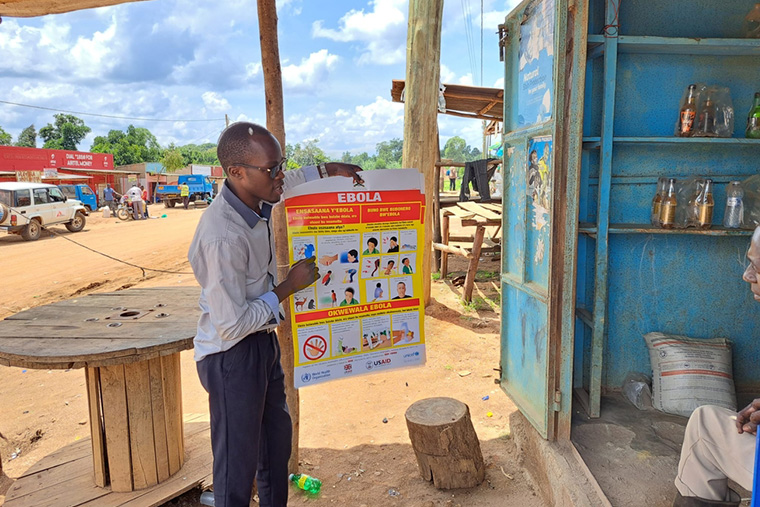 ムベンデ県マドゥドゥで、店の店主と話すMSFの健康推進担当者　Ⓒ MSF/Sam Taylor