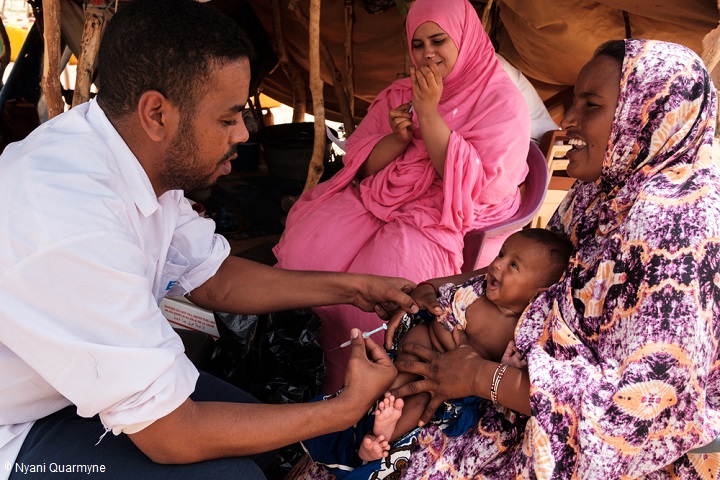 村を訪れ、農場で予防接種を行うMSF看護師と、お母さんに抱かれたモハマドちゃん（生後4ヵ月）