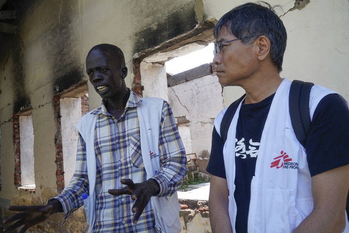 武力衝突によって破壊された病棟の前で現地スタッフから話を聞くいとうせいこう氏（南スーダン・マラカル、2018年11月撮影）© Toru Yokota