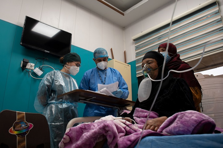 © Hassan Kamal Al-Deen/MSF<br> イラク・バグダッドの病院で酸素療法を受けている、新型コロナウイルス患者の高齢女性。MSFの看護師が患者の状態を確認し、家族にサポートの方法を説明している。