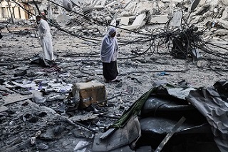 がれきと化した建物の前に立つ女性<br> 🄫 MOHAMMED ABED / AFP