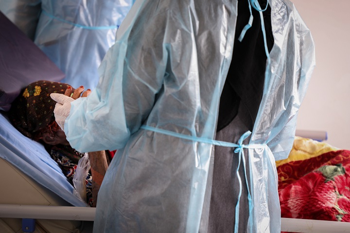 高齢女性の手を握って介抱するMSFコロナ治療センターの看護師 © MSF/Majd Aljunaid