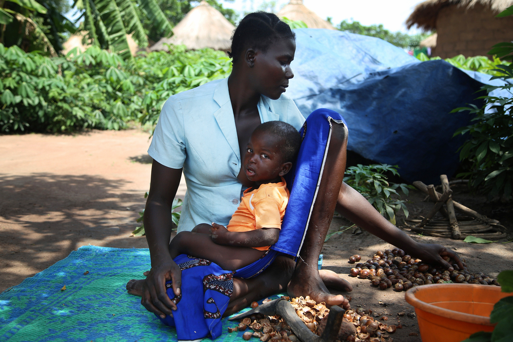 避難民の住む居住区で、子どもを抱きながらシアの実をむく女性 © Igor Barbero/MSF