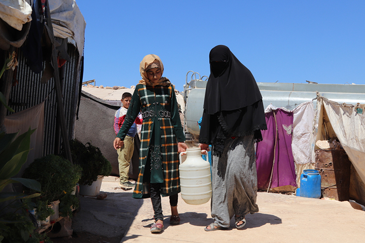 シリア北西部の避難民キャンプで、MSF提供の清潔な水が入った容器を運ぶ女性 © Abdurzaq Alshami