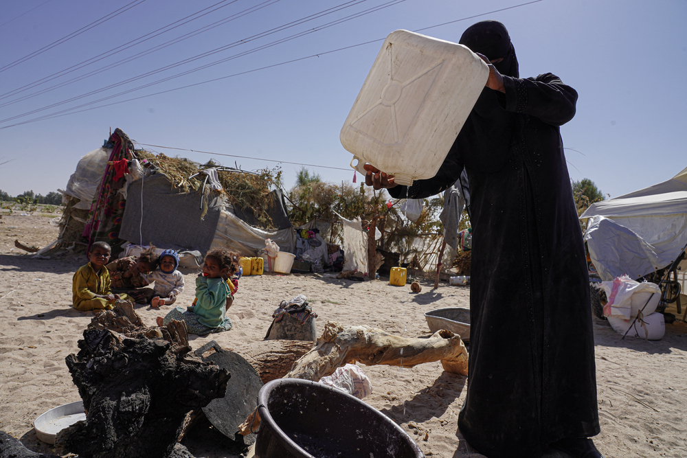 水タンクから最後の一滴の水を注ぐ女性。避難民キャンプでは水の確保も困難だ　© Hesham Al Hilali