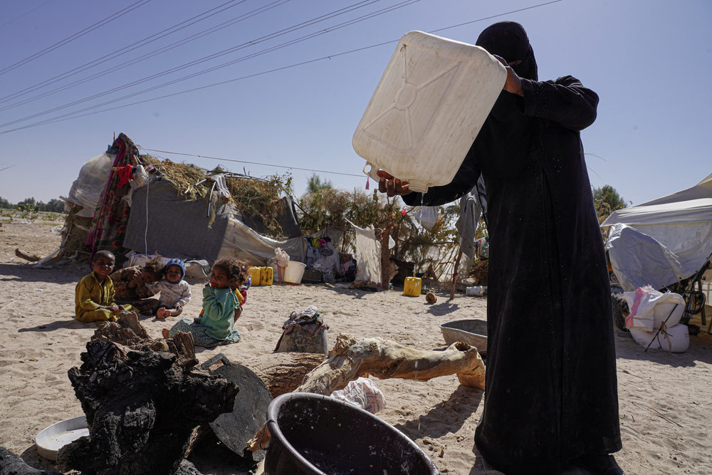 水タンクから最後の一滴の水を注ぐ女性。避難民キャンプでは水の確保も困難だ © Hesham Al Hilali