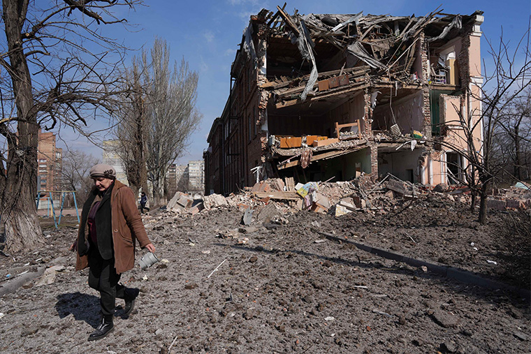 空爆で破壊された建物の前を歩く女性＝2022年3月13日　Ⓒ Evgeniy Maloletka/AP Photo