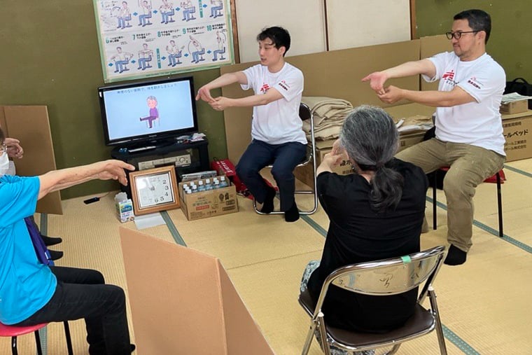 福島（右奥）とMSFの理学療法士（中央奥）が講師となり、参加者と一緒に簡単なストレッチをした＝熊本県八代市の避難所で　© MSF