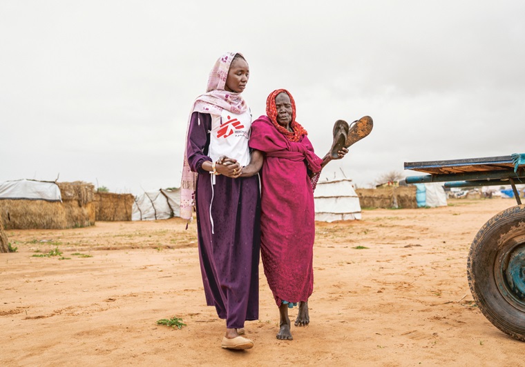 80歳になる女性の手を取って、MSFの診療所に向かうアイシャ（左）　Ⓒ Ante Bussmann/MSF