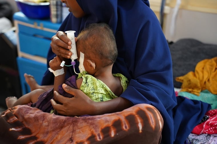 国境なき医師団（MSF）が支援するベイ地域病院で、栄養失調の我が子を抱き、注射器から栄養を与える母親＝2025年6月25日　© Hareth Mohammed/MSF