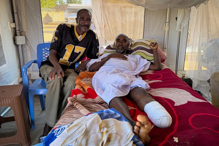 エル・ファシールで銃撃を受け、脚を切断したIAさん（右）。兄がロバ車でタウィラまで運んでくれた＝タウィラ病院で2025年11月9日　Ⓒ Natalia Romero Peñuela/MSF