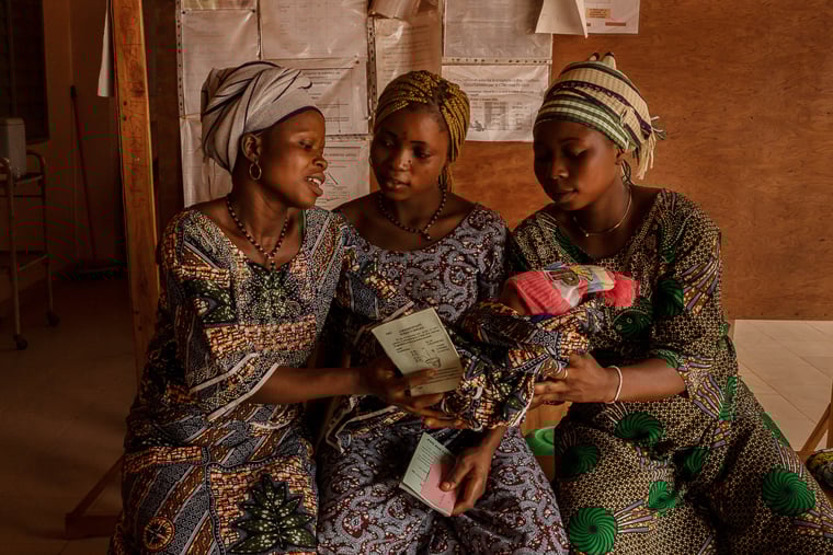 ベナン／クフォ県：自宅で3日前に1人で出産したオルタンスさん（左）。クルエカンメ診療所で診察を待つ間、生まれて間もない乳児を妊娠6カ月のメラニーさん（右）に手渡している＝2025年1月　© Adrienne Surprenant