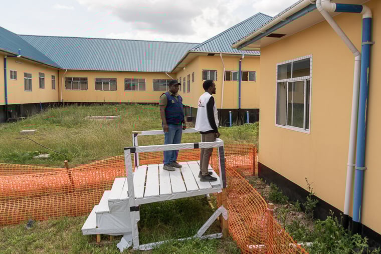 タンザニア／カゲラ地方：マールブルグ病の疑いがある患者の病棟を、保健省の緊急対応責任者マイケル・ケレメジ医師（左）と、MSFの医師フロリアン・D・ムワベサが巡回している。MSFは大きな窓付きの施設を建てることで、医療スタッフが感染リスクを負わずに患者を確認できるようにするとともに、家族が外から面会できるよう工夫した＝2025年2月　© Florence Dozol/MSF