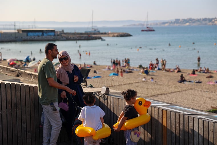 フランス：マルセイユの浜辺を見つめるイマドさんと妻、そして3人の娘たち。イマドさんはガザで9年間、MSFの医療チームリーダー兼看護活動マネジャーとして働いていたが、2025年3月に家族とともにガザからフランスへ避難した。娘の一人は心臓病を抱えており、2023年10月の紛争激化以前から医療搬送を待っていた＝2025年6月　© Mohammad Ghannam/MSF