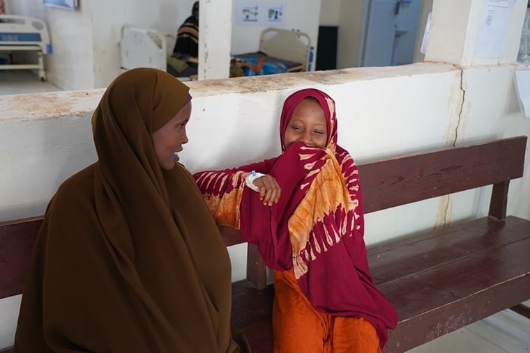 ソマリア／バイドア：母親の隣に座り、笑顔を隠すアミナさん（右）。ここはベイ地域病院で、彼女は1型糖尿病の治療のため、定期的に健診を受けている＝2025年6月　© Hareth Mohammed/MSF