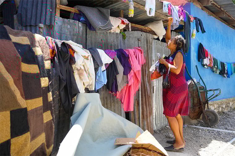 ハイチ／ポルトープランス：首都の各地で続く激しい暴力により家を追われた女性が、小さな避難所の屋根に干していた衣服を取り込んでいる＝2025年5月　© Marx Stanley Léveillé/MSF