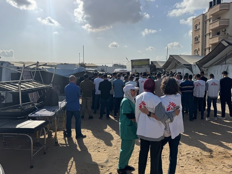 パレスチナ／ガザ地区：ナセル病院の外で大勢の人びとが祈りを捧げる中、MSFスタッフのアブドルハミド・カラダヤの遺体が葬儀のため墓地へ向かう救急車に運び込まれる。MSFにて18年間勤務し、理学療法活動マネジャーを務めていたアブドルハミドは、勤務先へ向かうバスを待つ路上でイスラエル軍の攻撃を受け殺害された。また、同僚のオマル・ハイエクも同日の攻撃で殺された。2023年10月以降にガザで殺害されたMSFスタッフは、オマルが14人目、アブドルハミドが15人目となった＝2025年10月　© Nour Alsaqqa/MSF