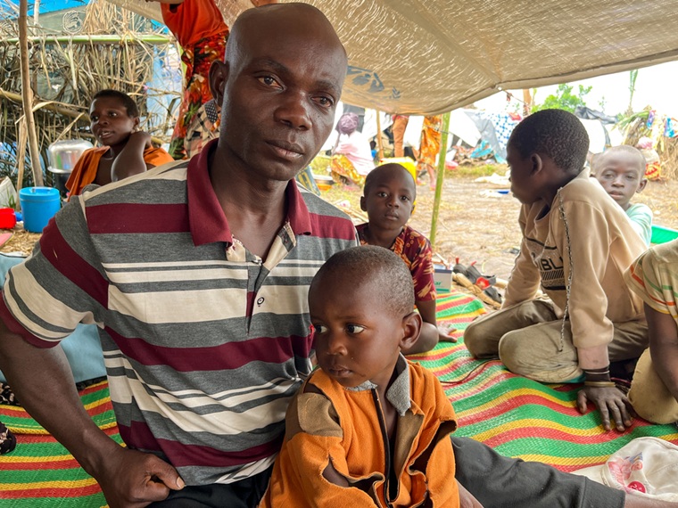 ンダバ・キャンプで他の家族と共に一枚の防水シートの下で暮らす親子。「雨に打たれ、食べものもお金もない」と父親は言う＝2025年12月16日　© Dorine Niyungeko/MSF