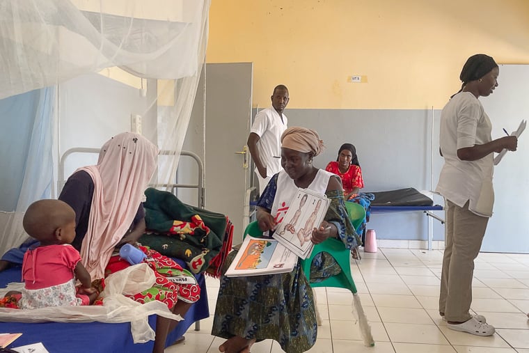 チャド東部アム・ティマン病院。ヘルスプロモーター（中央右）が絵本を使って患者の親子（左）に健康教育をしている＝2025年11月7日　©  Aichata Diakité/MSF