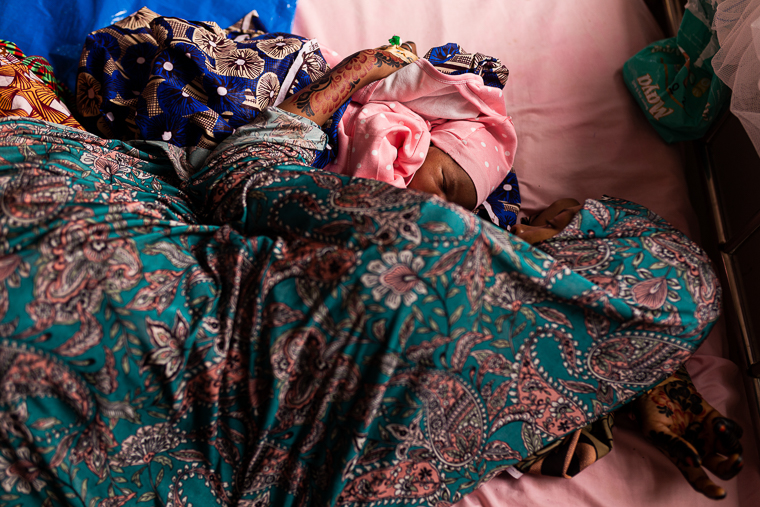 シンカフィ総合病院で出産したばかりの27歳の女性。ベッドの上で赤ちゃんを抱き、横たわっている＝2025年9月1日　© Nnoli Amarachi