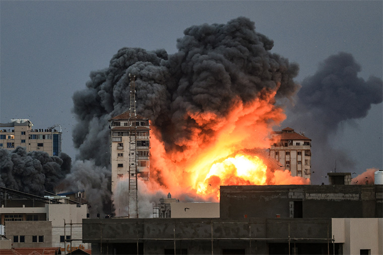 2023年10月7日、ガザ市でイスラエル軍の空爆を受けたパレスチナ・タワーから立ち上る炎と煙を見つめる人びと＝2023年10月7日　© Mahmud Hams/AFP