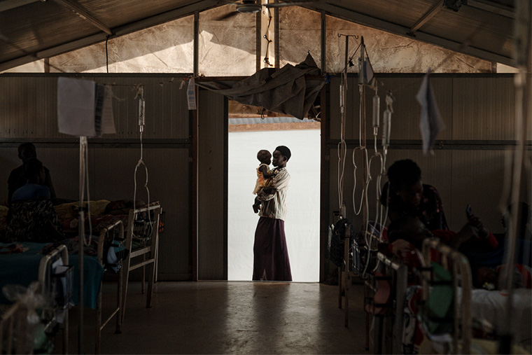 南スーダンのキャンプで病気の妹を抱く女性 © Sean Sutton