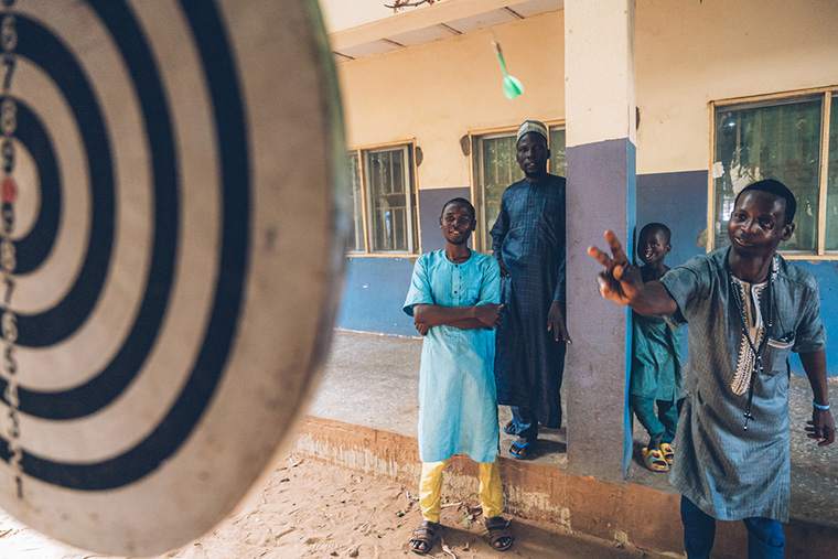 ナイジェリア：ソコト水がん（すいがん）病院の中庭でダーツに興じる、水がん患者のラビウさん（右）。この病院は水がん患者にとって、かけがえのない治療と癒しの場になっている。ラビウさんはMSFの医療チームから再建手術を受けた＝2023年5月　Ⓒ Fabrice Caterini/Inediz
