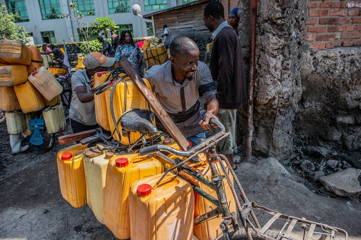 生活に必要な水の入ったいくつもの容器を運ぶ男性　© Moses Sawasawa