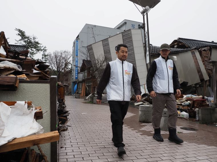 輪島市街で活動に向かうMSF心理士の福島正樹(左)とプロジェクト・コーディネーターの川邊洋三。輪島市内では、路上のがれきは片付いたものの、倒壊した建物はほとんど手つかずのままだ © MSF