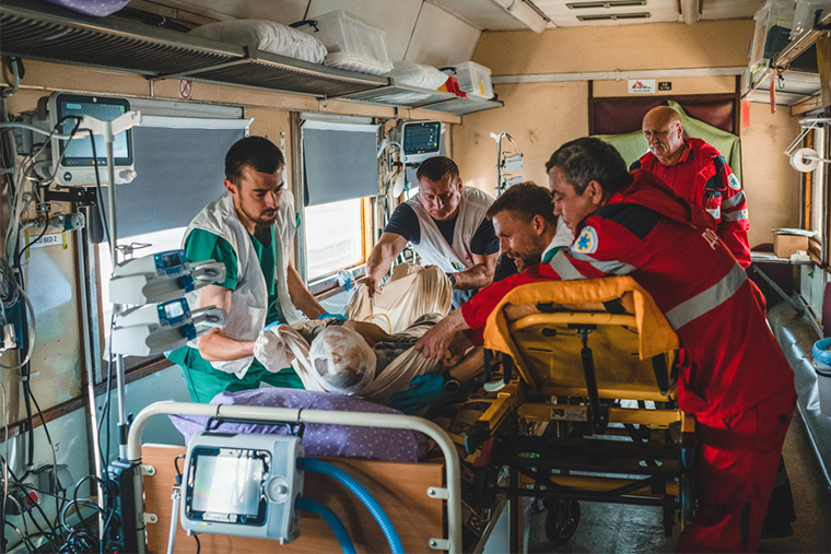 ウクライナ東部から西部のリビウまで戦傷者や重病の患者を搬送するMSFの医療列車。車内に設置された集中治療室で救急車の担架から患者をベッドに移す＝5月20日　© Andrii Ovod