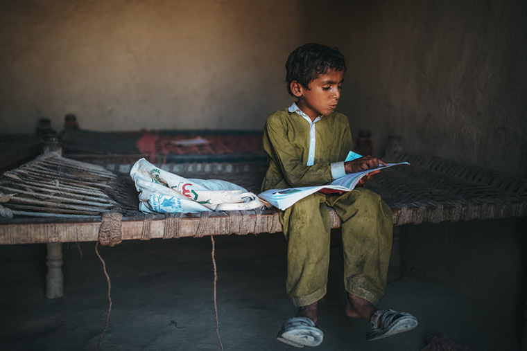 教科書を読む少年。大雨で家が倒壊したため、家族6人で1部屋のシェルターに暮らす。パキスタンの豪雨による洪水の被害は大きく、何カ月にも及ぶ恐れがある＝2022年10月　Ⓒ Asim Hafeez